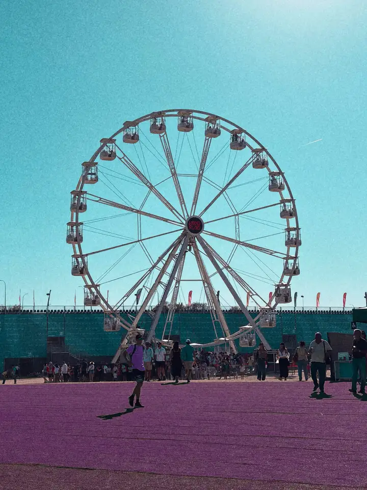 A Ferris wheel over a fairground beneath a bright cyan sky