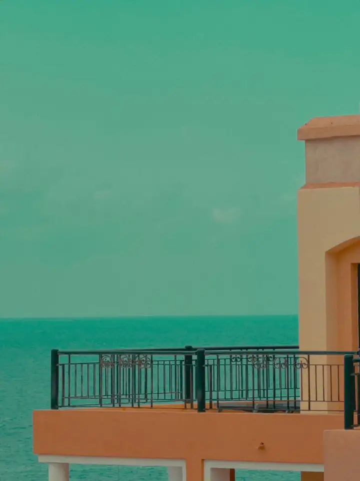 A peach-coloured balcony and railing beneath a turquoise sky