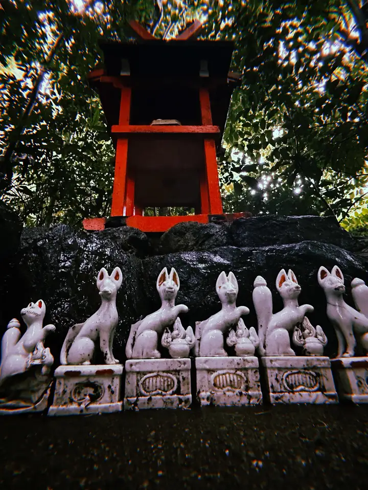 A red shrine gate behind a row of white fox statues