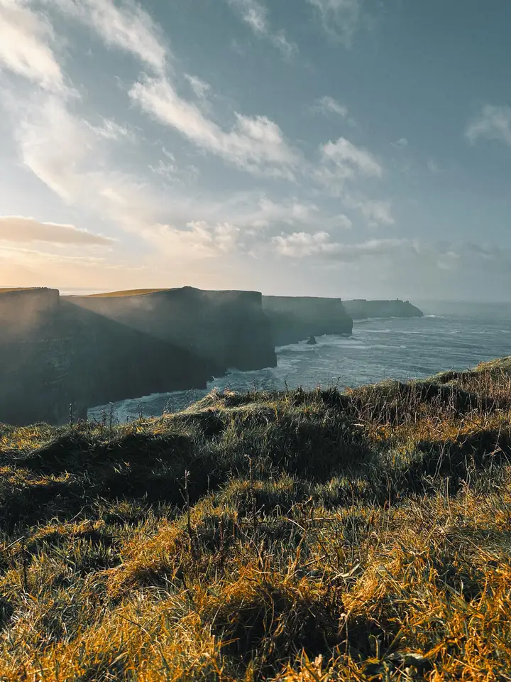 Grassy coastal cliffs above the sea beneath a cloudy sky