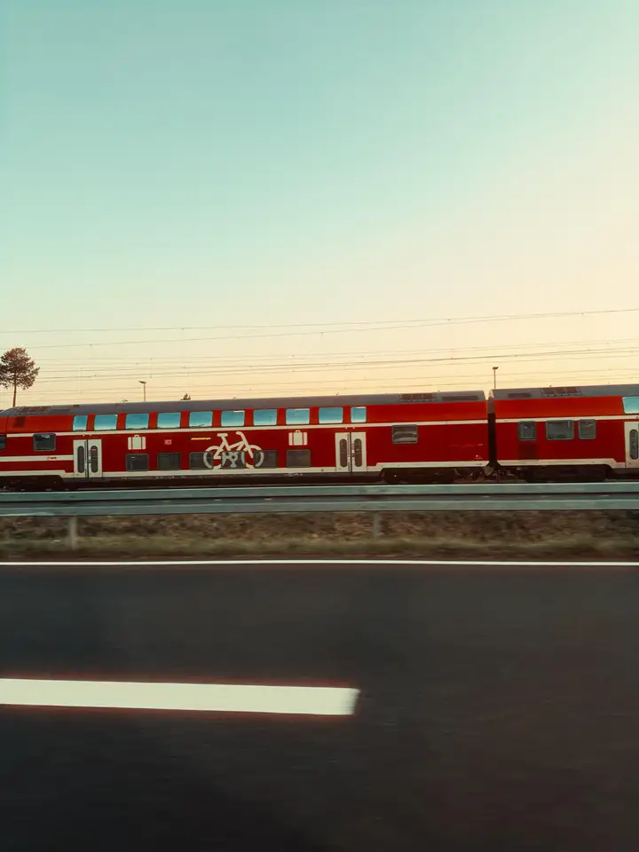 A red train beyond a dark road under a pale mint sky
