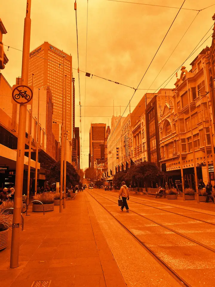A pedestrian on a quiet city street beneath an orange sky